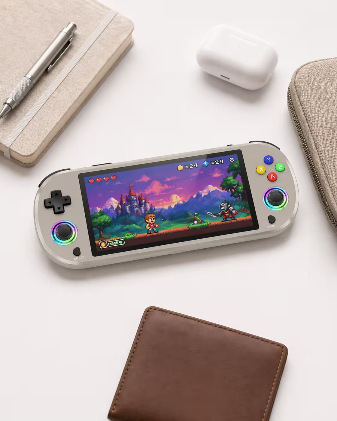 iGameConsole M22 Pro warm gray compact retro handheld console beside everyday carry items including a notebook, pen, earbuds case, wallet, and pouch, showing portable size and modern retro gaming style.