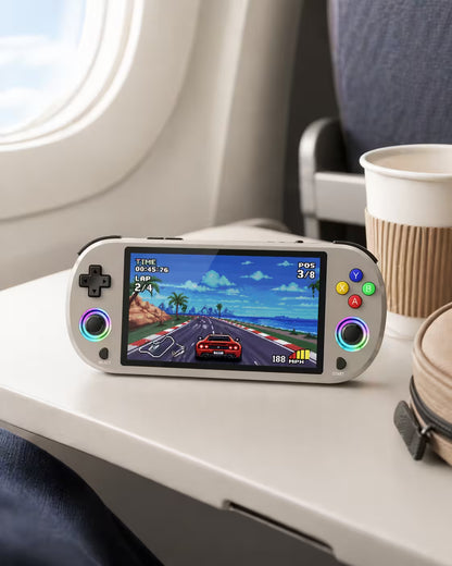 iGameConsole M22 Pro warm gray portable gaming console on an airplane tray table with a coffee cup and travel bag, showing retro gaming on the go.