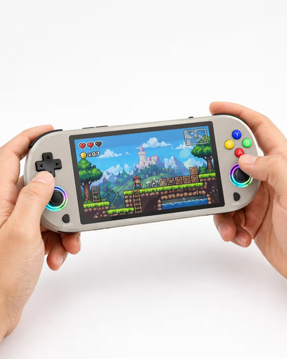 Adult hands holding the iGameConsole M22 Pro warm gray portable handheld console, showing its compact horizontal design, comfortable grip, RGB-ring joysticks, D-pad, and colorful retro platform game screen.