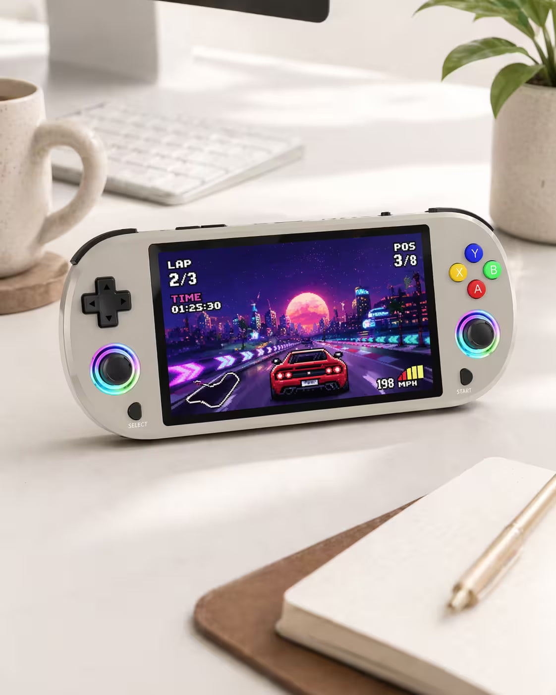 iGameConsole M22 Pro warm gray retro portable console on a clean modern desk setup with a notebook, coffee mug, plant, keyboard, and colorful pixel racing game screen.
