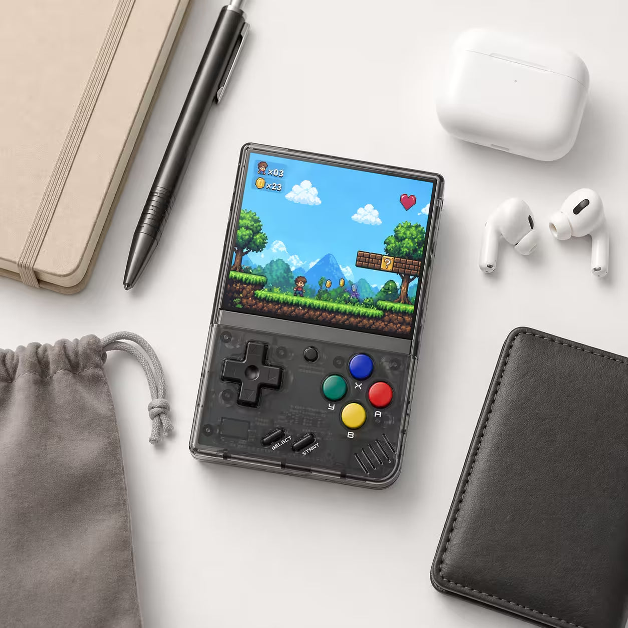 iGameConsole MIYOO Mini Plus transparent black compact retro handheld console beside everyday carry items including a pouch, notebook, pen, wallet, and earbuds case, showing portable size and retro gaming style.