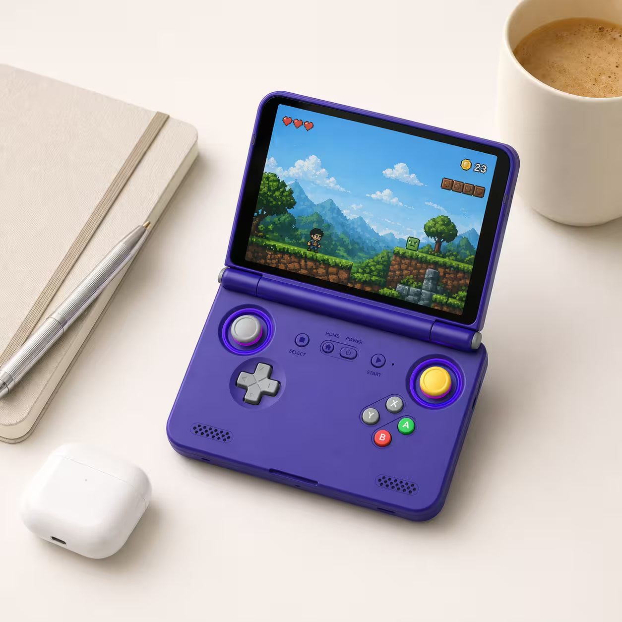 iGameConsole purple compact retro handheld console beside everyday carry items including a notebook, pen, wireless earbuds case, and coffee cup, showing portable size and retro gaming style.