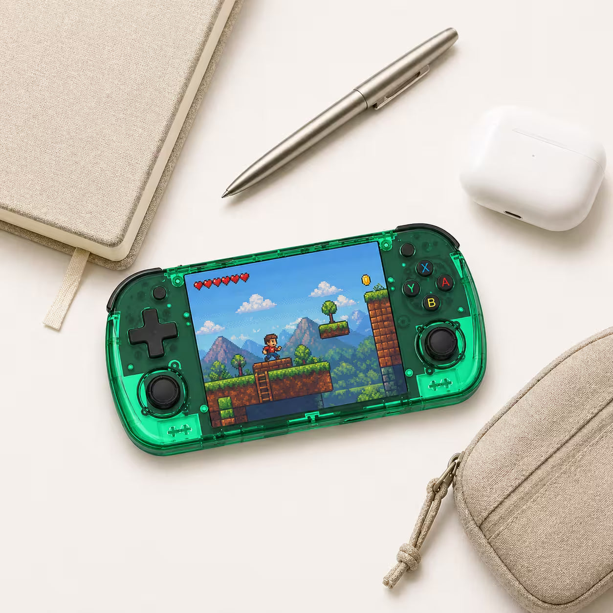 iGameConsole R36H Promax transparent green compact retro handheld console beside everyday carry items including a notebook, pen, earbuds case, and pouch, showing portable size and daily carry convenience.