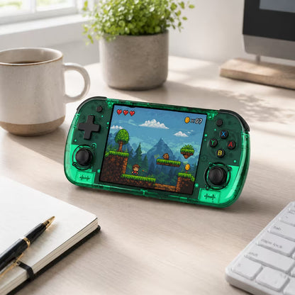 iGameConsole R36H Promax transparent green retro portable console on a clean modern desk setup with a coffee mug, notebook, keyboard, and plant, displaying a retro platform game.