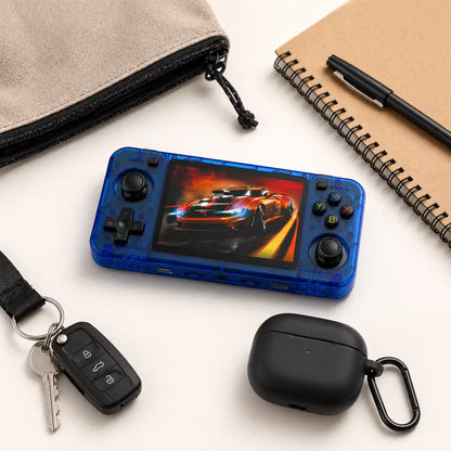 iGameConsole R36H transparent blue compact retro handheld console beside everyday carry items including a notebook, pen, earbuds case, wallet, and pouch, showing portable size and daily carry convenience.