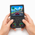 Adult hands holding the iGameConsole R36T MAX carbon fiber black portable handheld console, showing its compact vertical design, upper-left directional pad, ABXY buttons, dual RGB-ring joysticks, and colorful racing game screen.