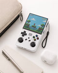 iGameConsole R36XX white compact retro handheld console beside everyday carry items including a pouch, notebook, pen, and earbuds case, showing portable size and daily carry convenience.