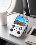 iGameConsole R36XX white portable gaming console on an airplane tray table with a coffee cup, passport, and travel pouch, showing retro gaming on the go.