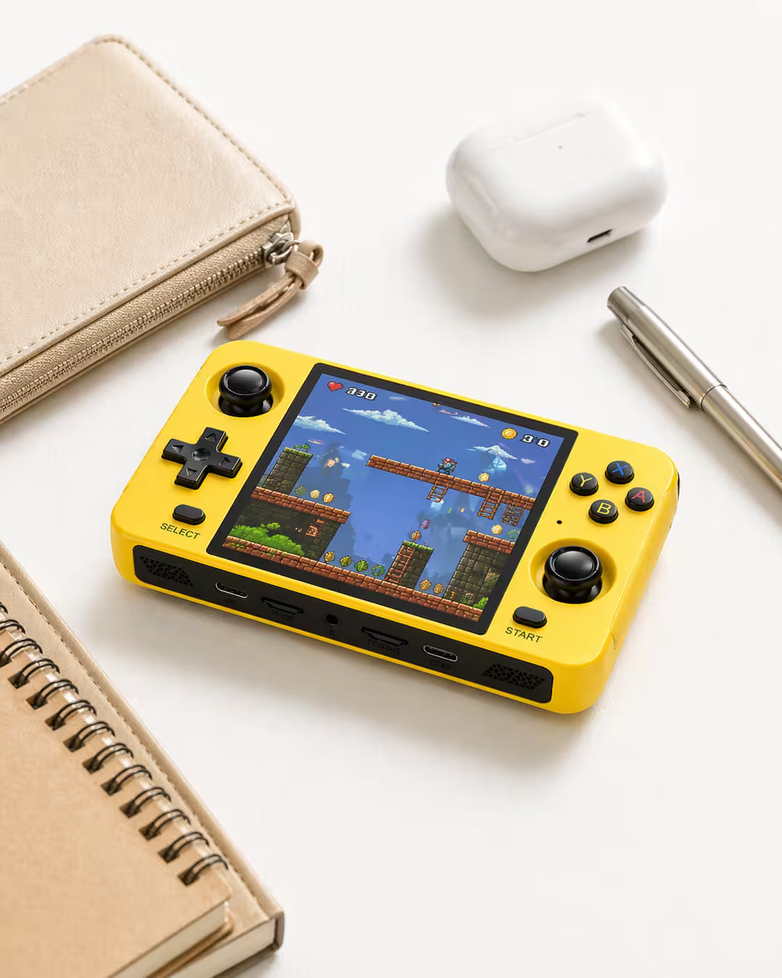 iGameConsole R40S bright yellow compact retro handheld console beside everyday carry items including a pouch, earbuds case, notebook, and pen, showing portable size and gaming-ready design.