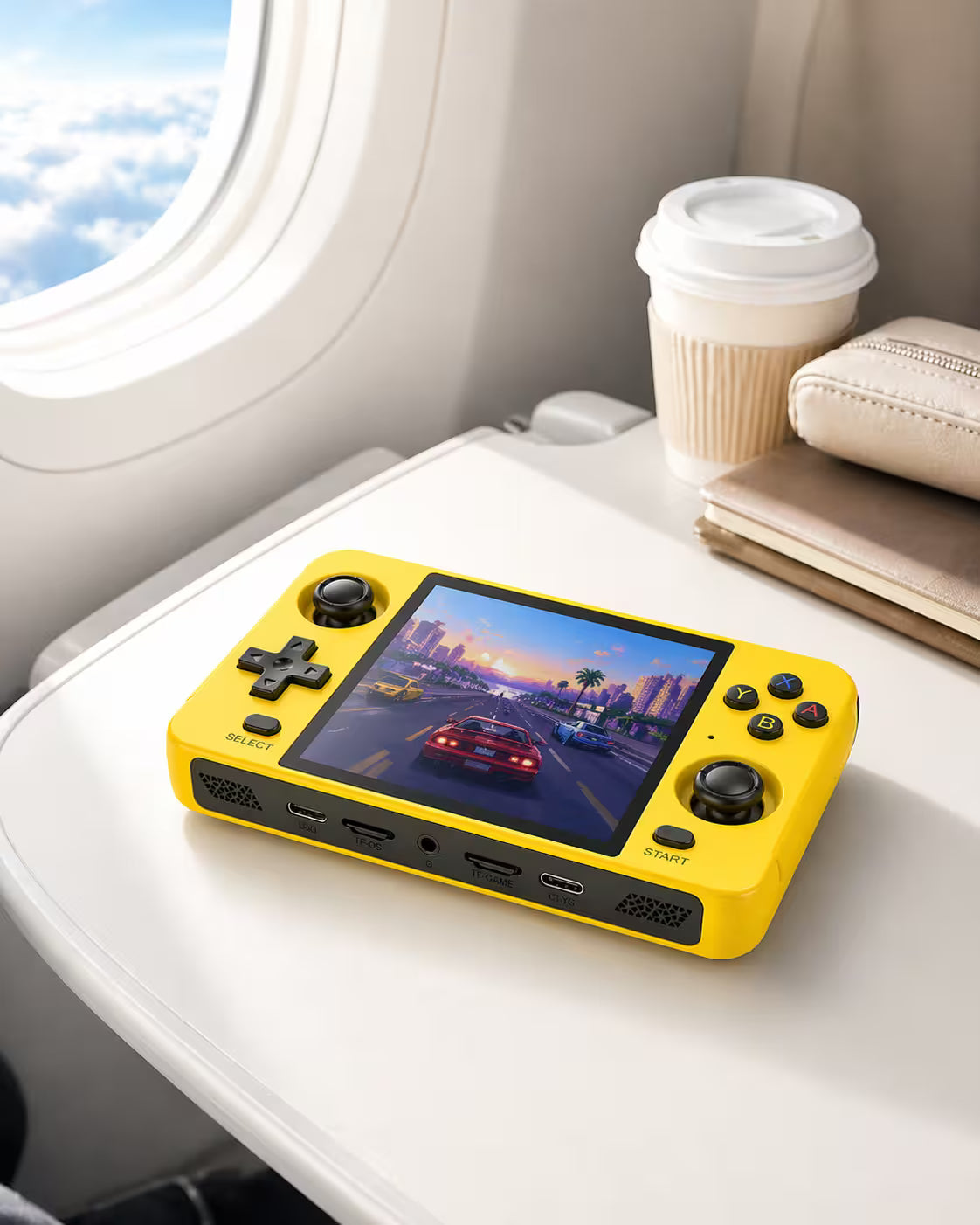 iGameConsole R40S bright yellow portable gaming console on an airplane tray table with a coffee cup and travel pouch, showing retro gaming on the go.