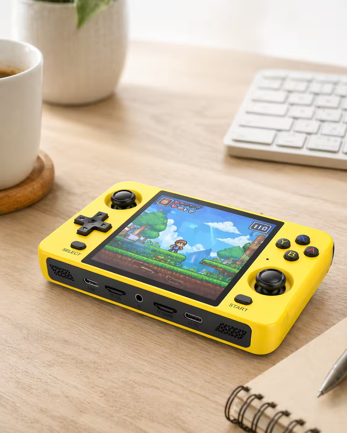 iGameConsole R40S bright yellow retro portable console on a clean modern desk setup with a keyboard, coffee mug, notebook, plant, and a colorful retro game screen.
