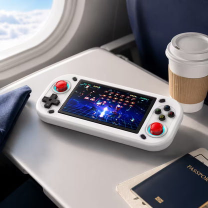 iGameConsole R43S white portable gaming console on an airplane tray table with a coffee cup and travel pouch, showing gaming on the go.