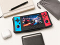 iGameConsole R50 Ultra black compact handheld console with cyan and red side panels beside everyday carry items including a notebook, pen, wallet, earbuds case, and pouch, showing portable size and gaming-ready design.