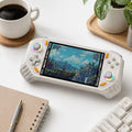 iGameConsole RG52 Pro Max off-white and orange retro portable console on a clean modern desk setup with a keyboard, coffee mug, notebook, and plant, displaying a colorful game screen.