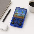 iGameConsole transparent blue compact retro handheld console beside everyday carry items including a notebook, pen, coffee cup, and earbuds case, showing portable size and retro gaming style.