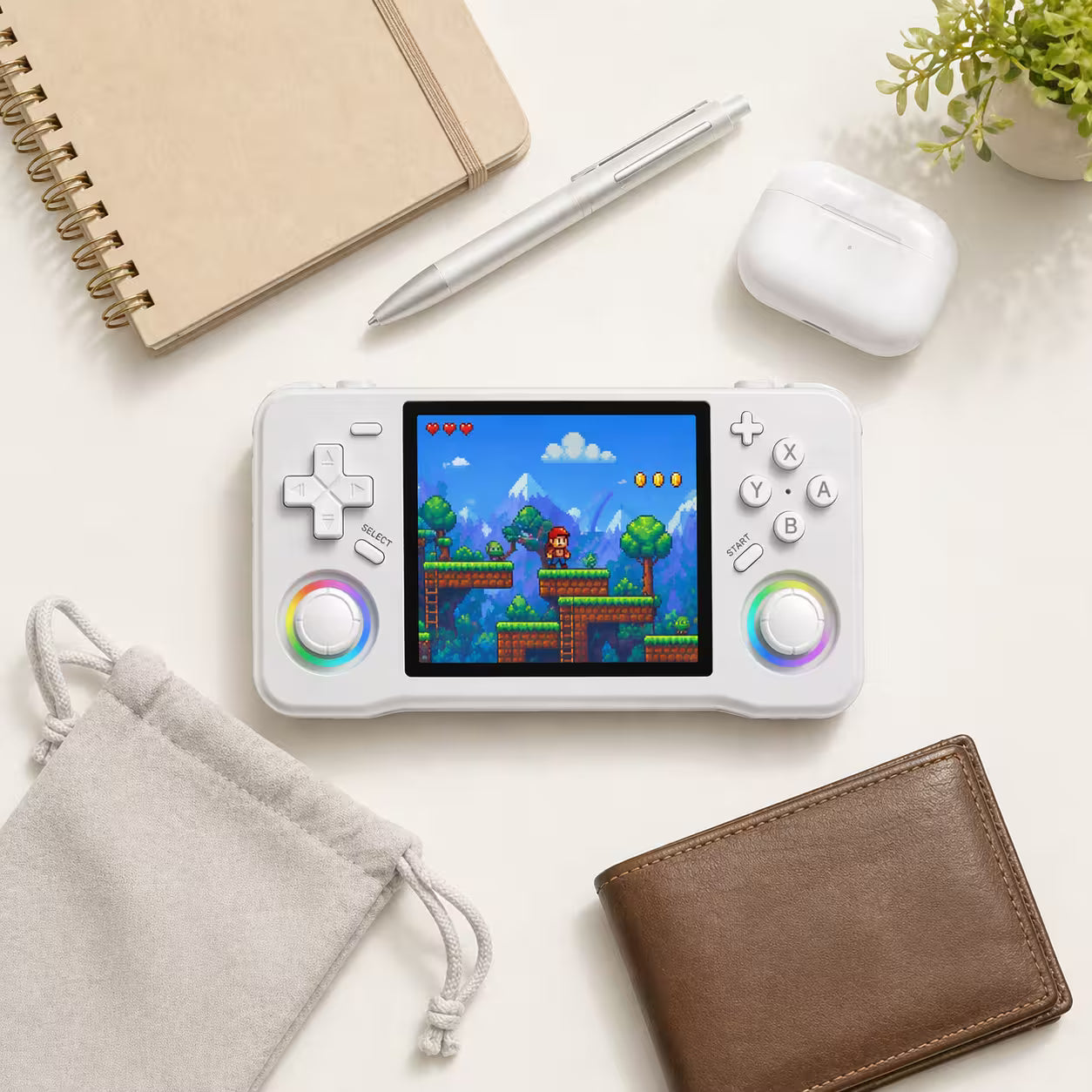 iGameConsole XF35H white compact retro handheld console beside everyday carry items including a pouch, notebook, pen, wallet, and earbuds case, showing portable size and modern retro gaming style.