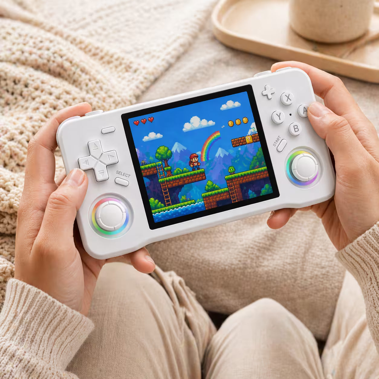 Adult hands holding the iGameConsole XF35H white portable handheld console, showing its compact horizontal design, comfortable grip, dual RGB-ring joysticks, D-pad, and retro platform game screen.