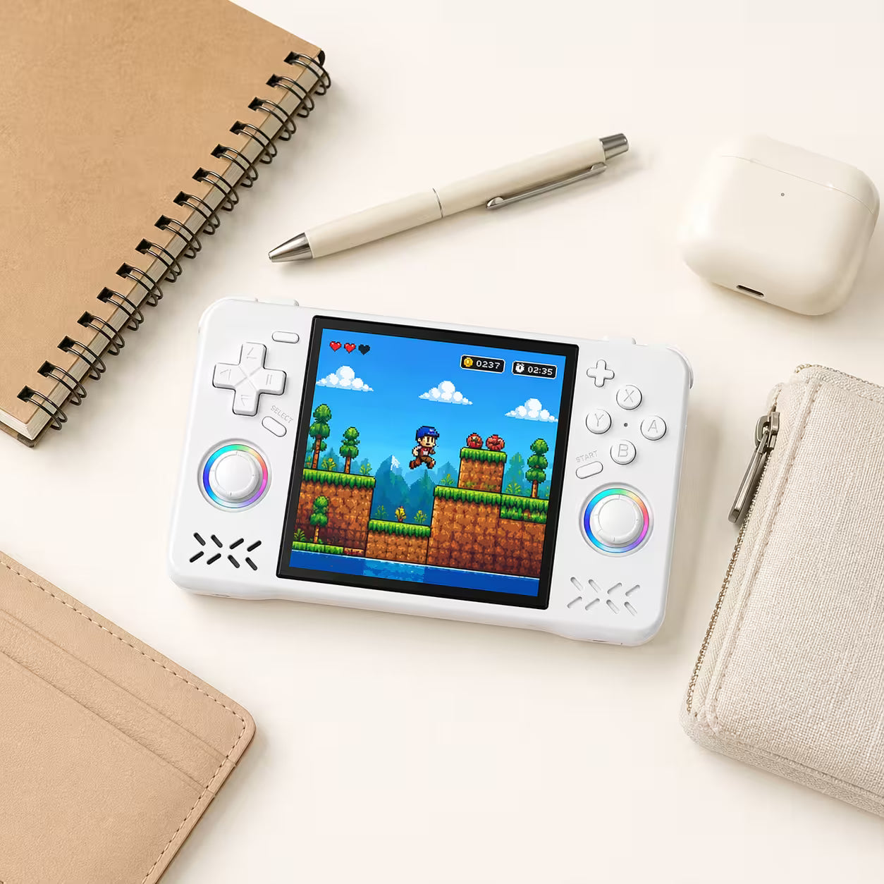 iGameConsole XF40H WiFi Pro white compact retro handheld console beside everyday carry items including a notebook, pen, earbuds case, wallet, and pouch, showing portable size and modern retro gaming style.