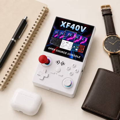 iGameConsole XF40V white compact retro handheld console beside everyday carry items including a notebook, pen, earbuds case, wallet, and watch, showing portable size and clean white design.